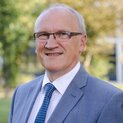 Ein Mann mit Brille steht lächelnd in einem Garten.