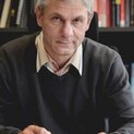 Ein Mann sitzt vor einem Bücherregal und schreibt in einen Terminkalender.