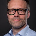 Ein Mann mit Brille und Bart schaut freundlich in die Kamera.