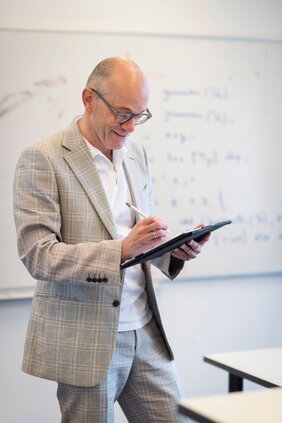 Porträt Professor Dr. Joost-Pieter Katoen. Der Informatiker schaut auf ein Tablet, das er in den Händen hält. 