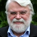 Ein Mann mit Vollbart und randloser Brille lächelt in die Kamera.