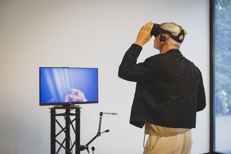 Ein Mann trägt eine VR-Brille. Vor ihm ist ein Bildschirm zu sehen.