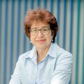 Eine Frau mit Brille steht vor einer gestreiften Wand.