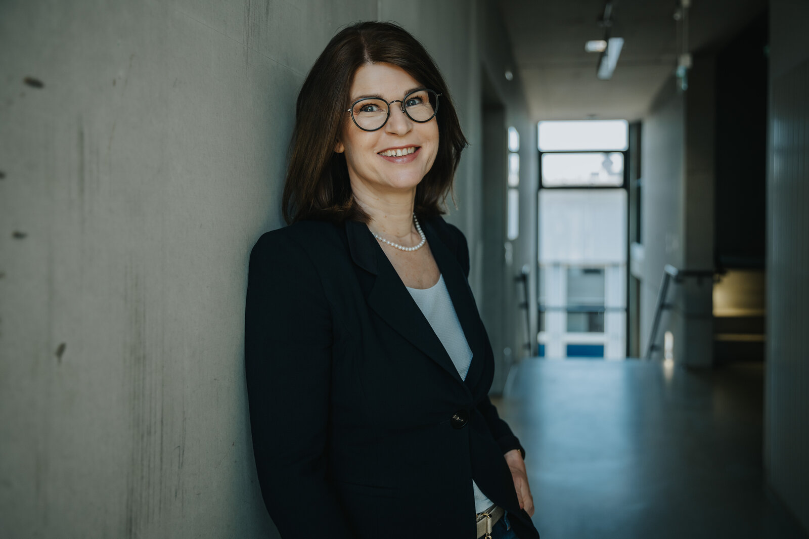 Frau mit Brille lehnt lächelnd an einer Wand.