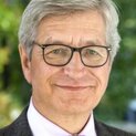 Ein Mann mit schwarzer Brille lächelt freundlich in die Kamera. 