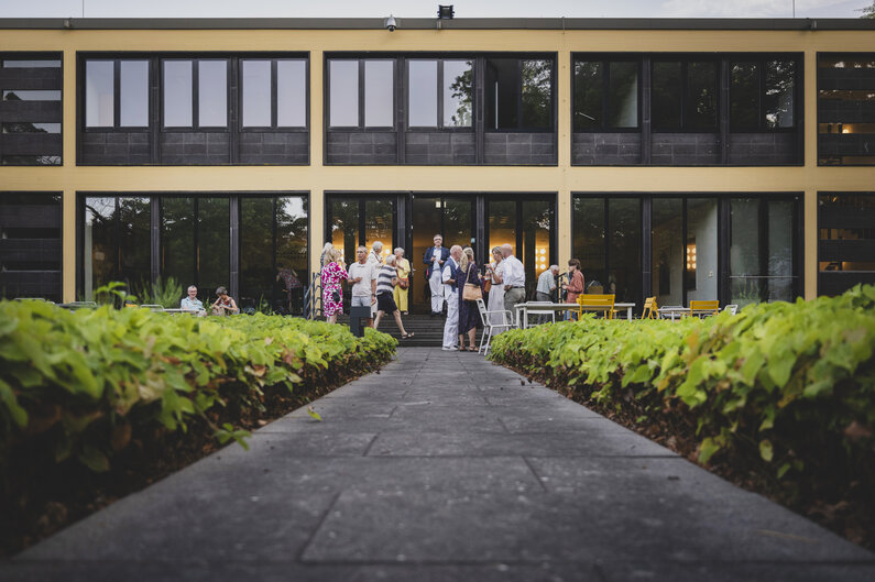 Menschen unterhalten sich im Garten vor dem Gebäude der Akademie. 