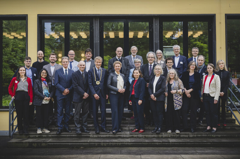 Elegant gekleidete Männer und Frauen haben sich für ein Gruppenfoto auf einer Treppe aufgestellt.