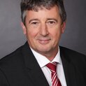 Ein Mann in Anzugjacke und mit Krawatte schaut lächelnd in die Kamera.