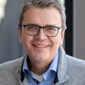 Ein Mann mit Brille lächelt strahlend in die Kamera.