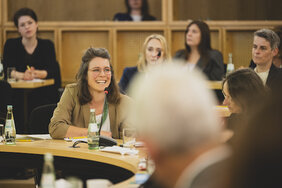 Nachhaltigkeitsforum 2024: Eine junge Frau lacht. Vor ihr auf dem Tisch steht ein Mikrofon. 