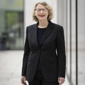 Eine Frau in einem schwarzen Kostüm lächelt in die Kamera.