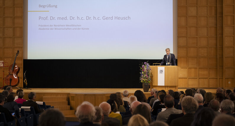 Ein Mann steht an einem Rednerpult. Im Hintergrund ist sein Name eingeblendet: Prof. Dr. med. Dr. h.c. Dr. h.c. Gerd Heusch.