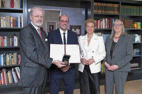 Zwei Männer und zwei Frauen haben sich für ein Foto aufgestellt. Einer der Männer hält eine Urkunde ins Bild. 