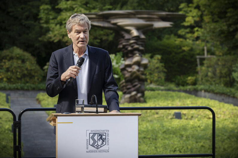 Im Garten der Akademie steht ein Mann an einem Rednerpult.