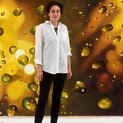 Eine Frau steht vor einer goldenen, künstlerischen Wand und lächelt.