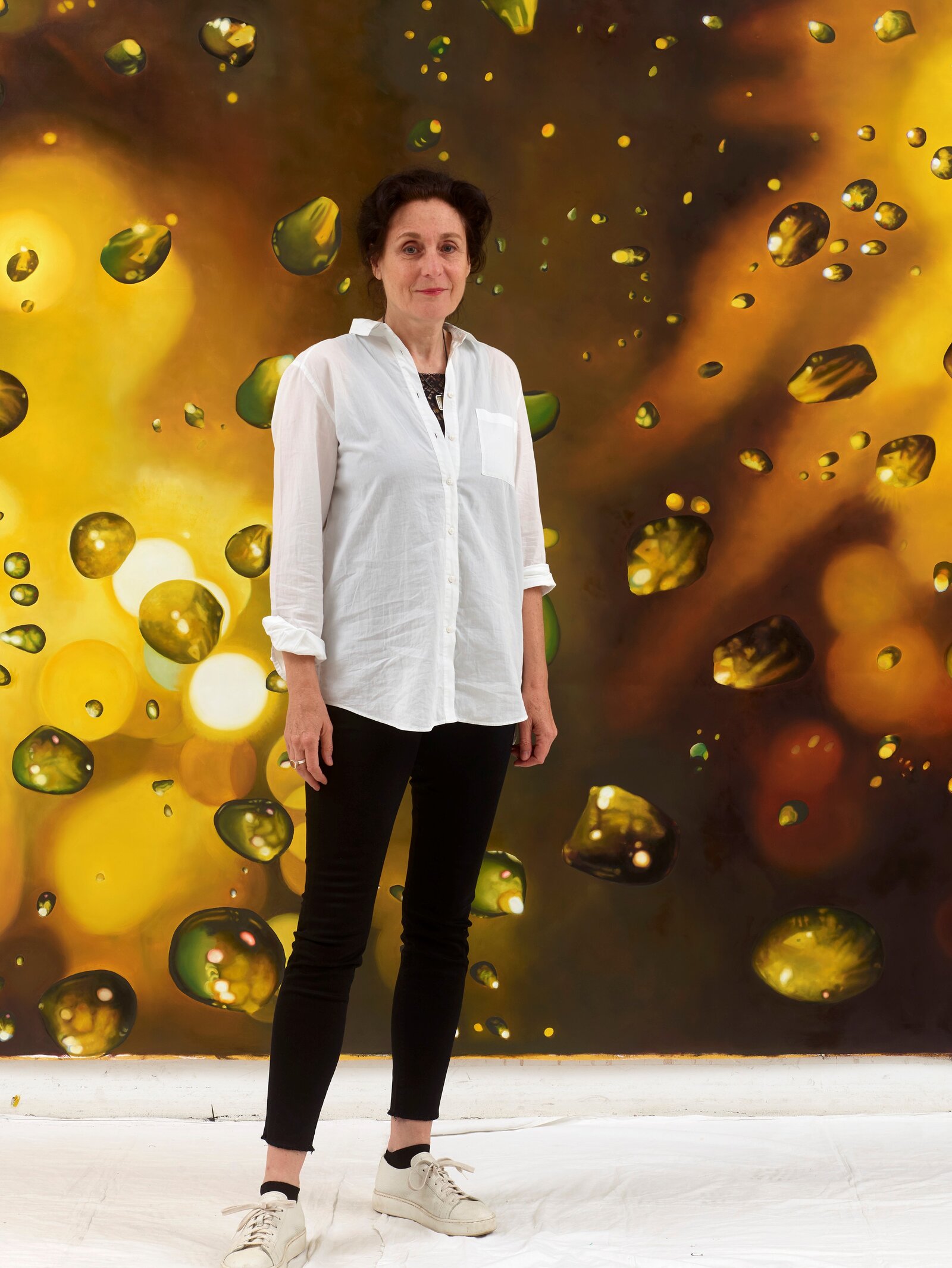 Eine Frau steht vor einer goldenen, künstlerischen Wand und lächelt.