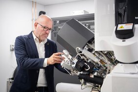 Porträt Professor Dr. Stefan Raunser. Der Biochemiker schaut durch ein Mikroskop.