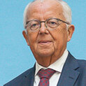 Ein Mann mit Brille schaut in die Kamera. Er trägt Anzug und Krawatte.