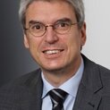 Ein Mann mit Brille und Krawatte lächelt in die Kamera.