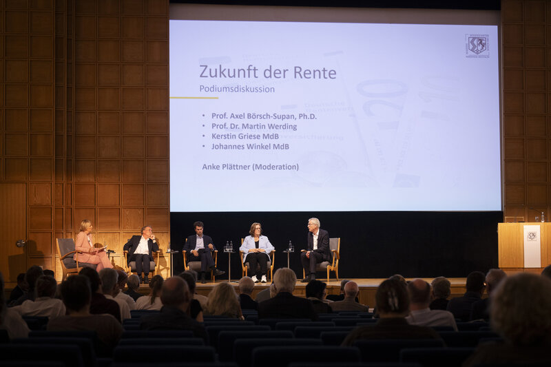 Zwei Frauen und drei Männer sitzen auf einem Podium. Auf der Leinwand hier ihnen ist der Titel der Veranstaltung eingeblendet: Zukunft der Rente.