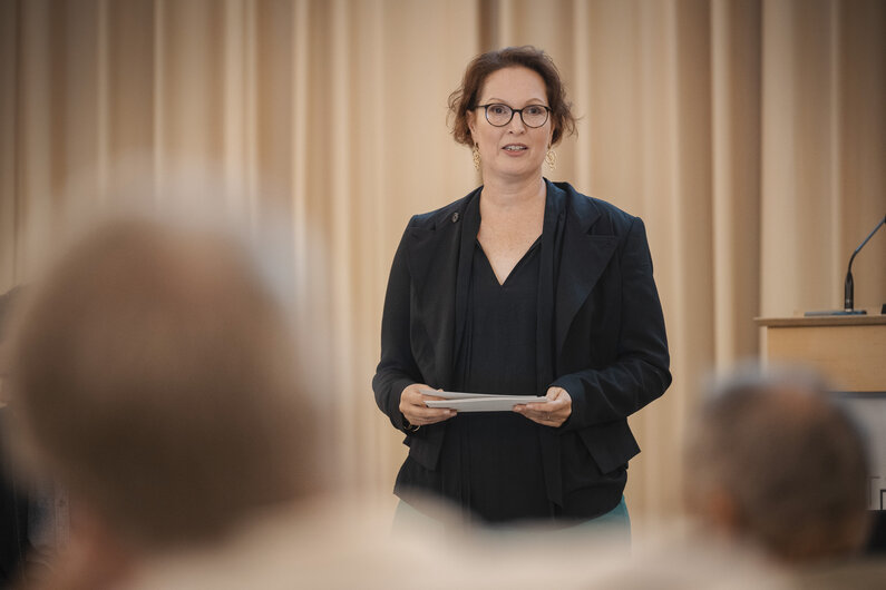 Eine Frau steht in einem Vortragsraum. In den Händen hält sie Moderationskarten. 