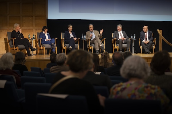 Drei Männer und drei Frauen sitzen auf einer Bühne. Einer der Männer hat ein Mikrofon in der Hand.