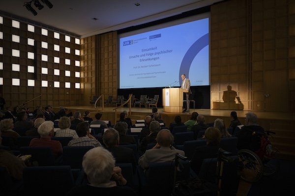 Ein gut gefüllter Veranstaltungssaal. Ein Mann hält einen Vortrag.