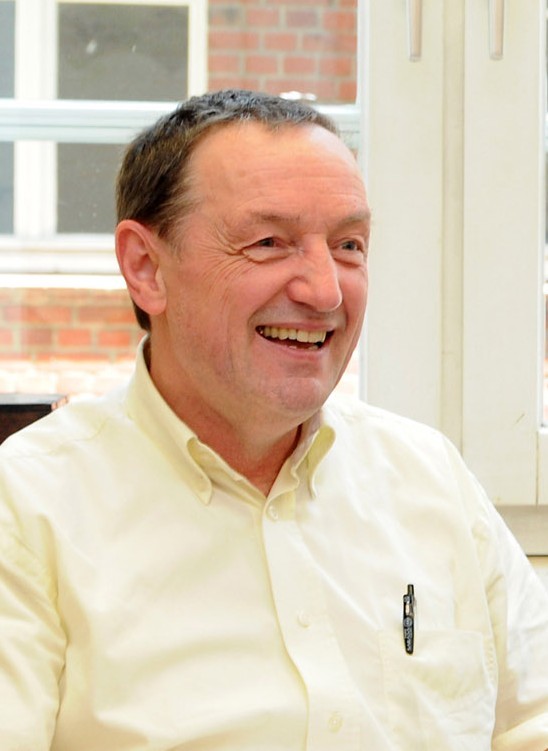 Ein Mann sitzt vor einem Fenster. Er schaut lächelnd nach rechts.