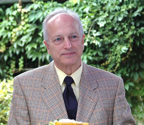 Ein Mann steht vor Sträuchern. Er lächelt und schaut nach halbrechts.