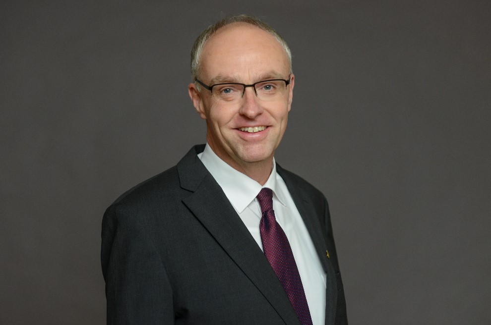 Mann mit Brille steht lächelnd vor einer Wand.