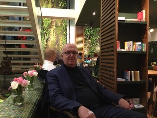 Mann mit Brille sitzt neben einem Bücherregal.