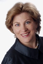 Frau mit Perlenkette lächelt in die Kamera.