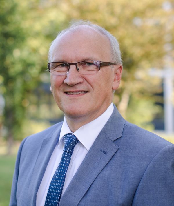 Ein Mann mit Brille steht lächelnd in einem Garten.