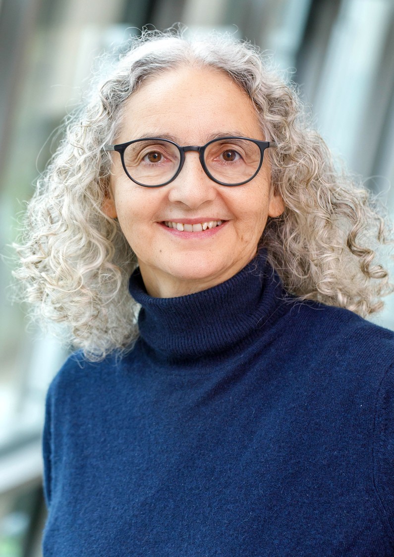 Eine Frau mit lockigem, langen Haar und Brille lächelt strahlend in die Kamera.
