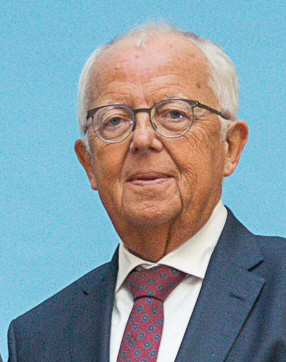 Ein Mann mit Brille schaut in die Kamera. Er trägt Anzug und Krawatte.